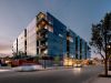 Optima Verdana luxury apartment with Modern glass apartment building at dusk, part of the Optima Community, with cars driving by and tree-lined streets.