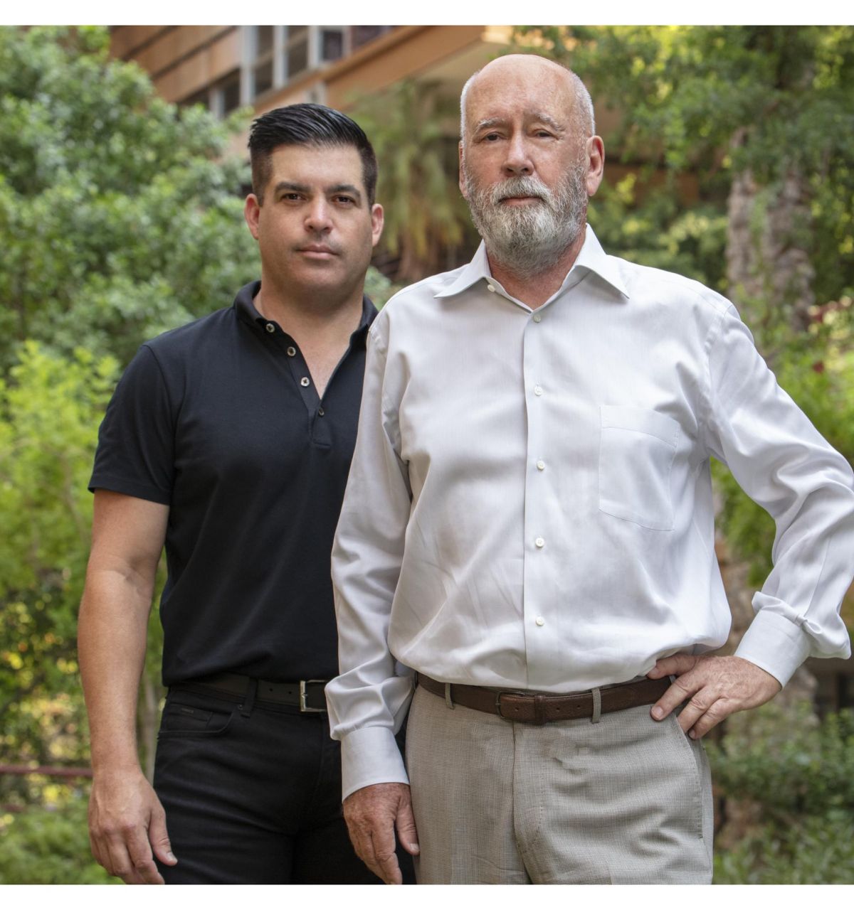 Two people in business attire standing next to each other with lush greenery is in the background at Optima Sonoran Village.