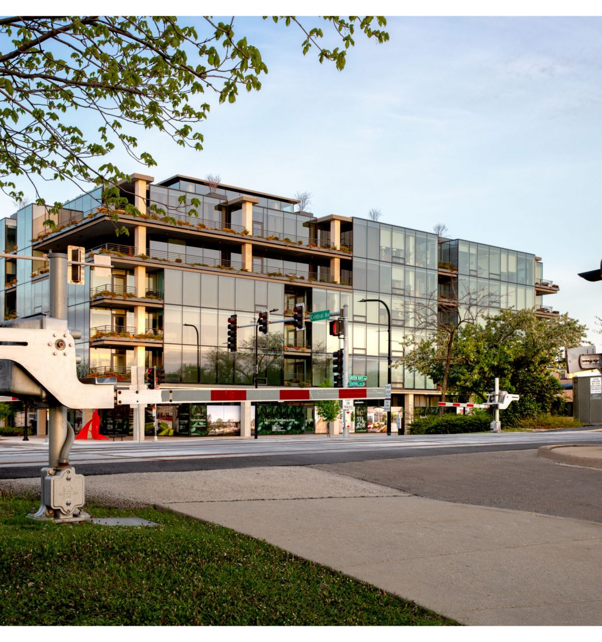 Optima Verdana luxury apartment with A modern glass building behind a lowered railroad crossing gate on a city street.