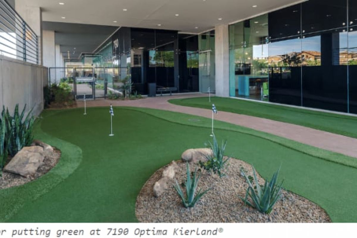Optima Verdana luxury apartment with Outdoor putting green with small plants and rocks beside a modern glass building, offering luxury home golf amenities in Optima communities.