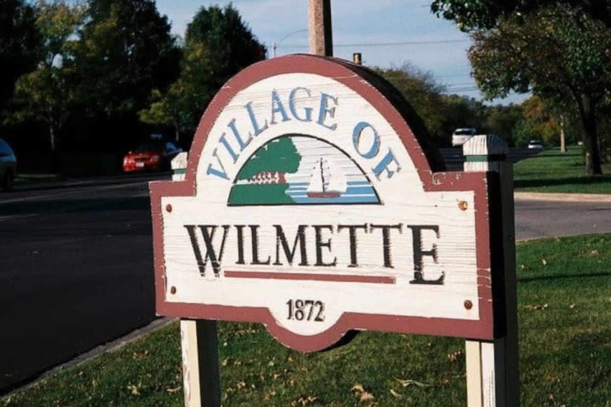 Optima Verdana luxury apartment with Wooden sign reading "Village of Wilmette 1872" with a sailboat, trees, street, and captured for the Wilmette Sesquicentennial Photography Project.