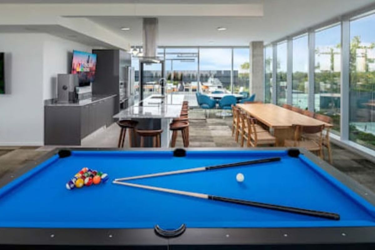 Optima Verdana luxury apartment with A modern game room with a blue billiards table, kitchen area, dining table, and large windows offering a city view.