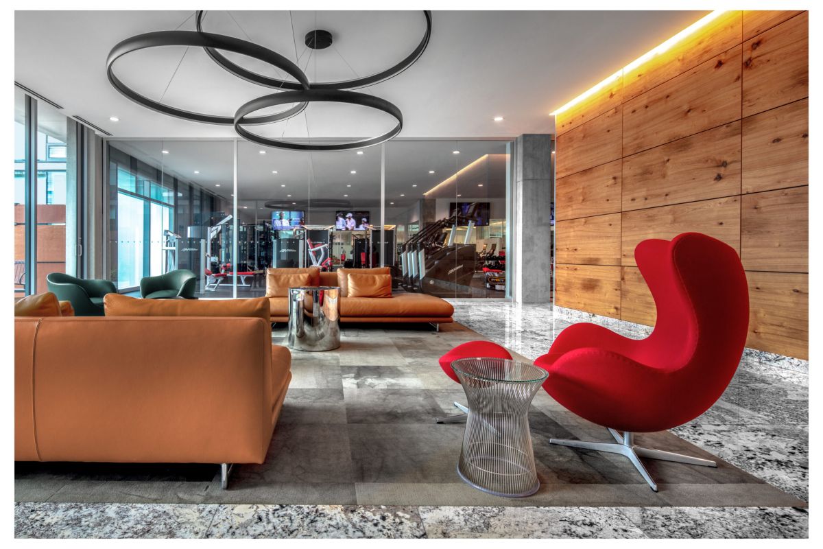 Optima Verdana luxury apartment with Modern lounge area at Optima Verdana with leather sofas, a red chair, and a glass wall showing the gym—built to last for years.