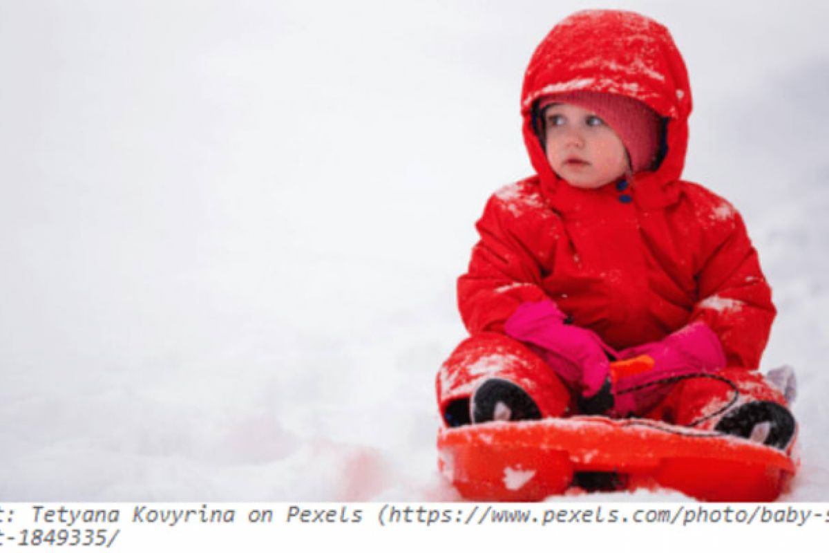 Optima Verdana luxury apartment with A young child in a red snowsuit sits on a sled, ready for winter fun on the snowy sledding hills.