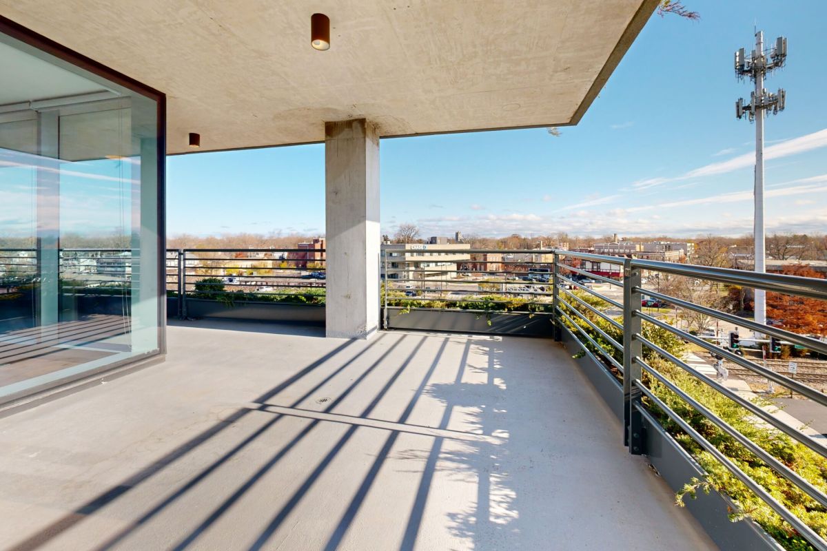 Optima Verdana luxury apartment with Sunny modern Optima balcony with metal railings, city view, and reflections on the glass doors enhance the inviting outdoor space.