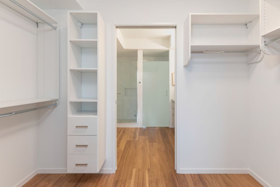 Optima Verdana luxury apartment with Spacious, empty walk-in closet with built-in shelves, drawers, and hanging rods, leading to a bathroom.