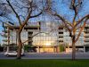 Optima Verdana luxury apartment with Modern glass apartment building reflected in evening light, framed by two leafless trees and a car driving by.