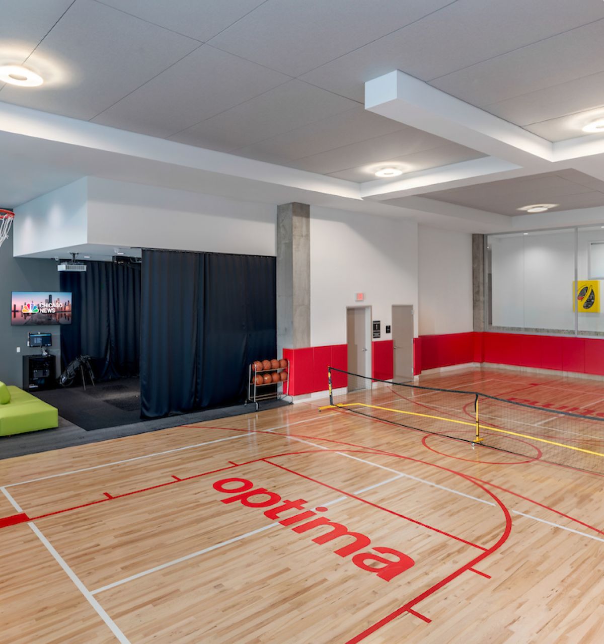 Optima Verdana luxury apartment with Indoor gym with basketball court, small tennis net, green couch, TV, and red and white walls.