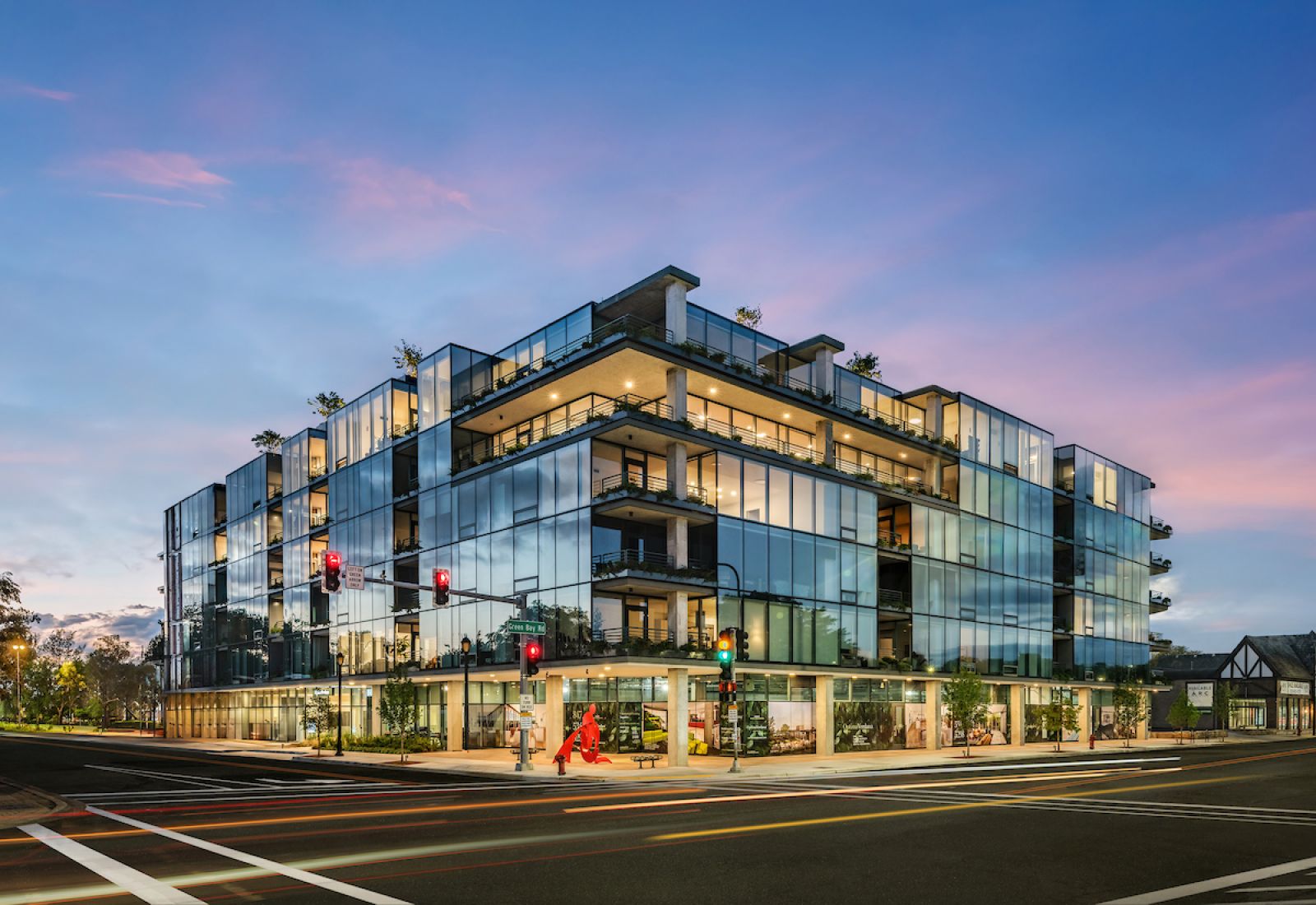 Optima Verdana luxury apartment with Modern glass building with balconies at a street corner during twilight, with traffic lights and a few pedestrians.
