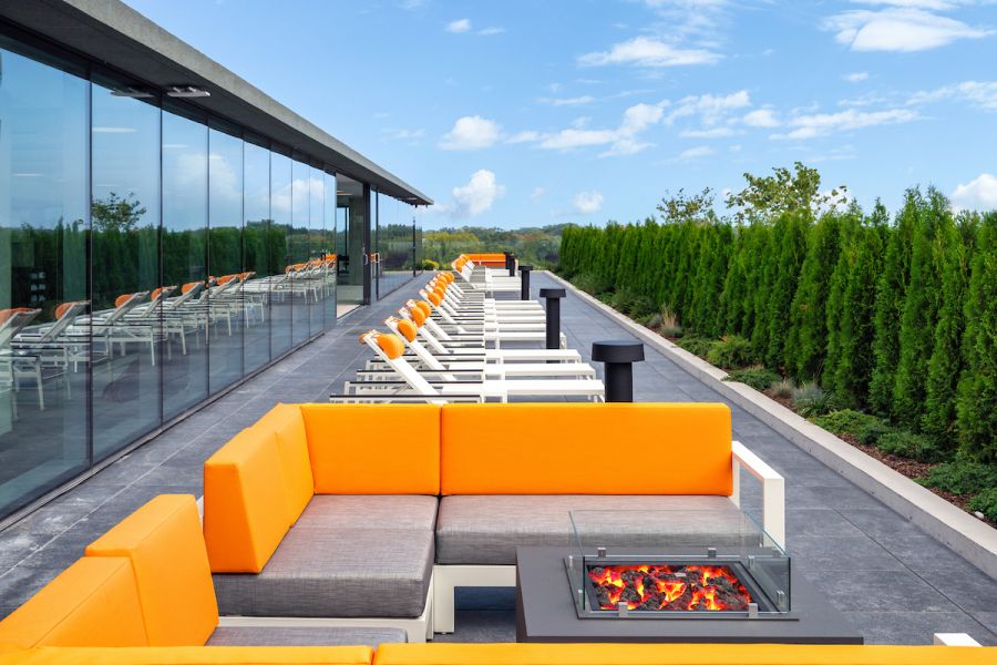 Optima Verdana luxury apartment with Modern rooftop patio with orange couches, lounge chairs, fire pit, and greenery under a blue sky.