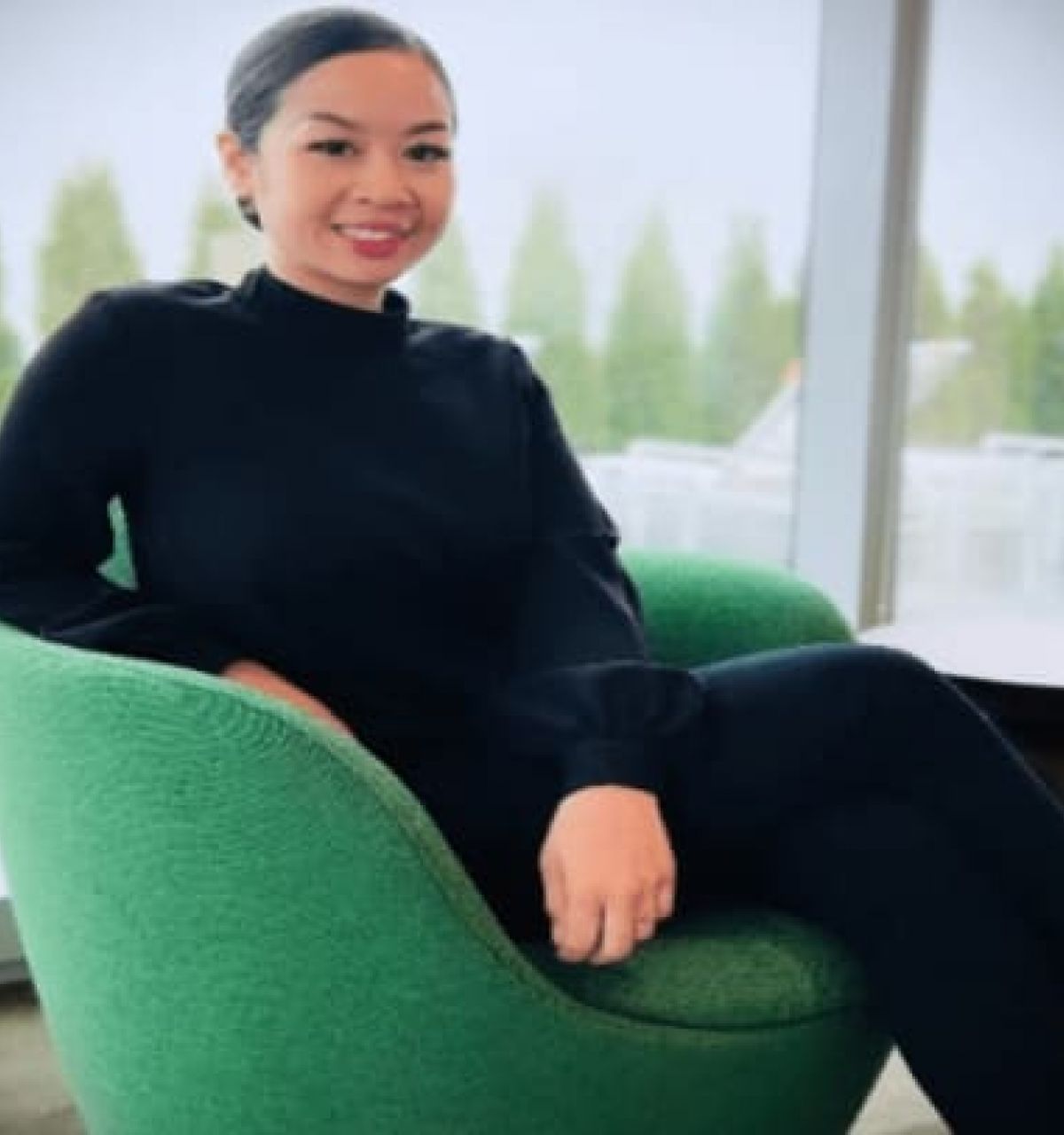Optima Verdana luxury apartment with Tracy Ratdavong sits smiling on a green chair in a modern, bright indoor space with large Optima Voices windows.