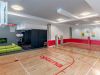 Optima Verdana luxury apartment with Indoor gym with basketball court, small tennis net, green couch, TV, and red and white walls.
