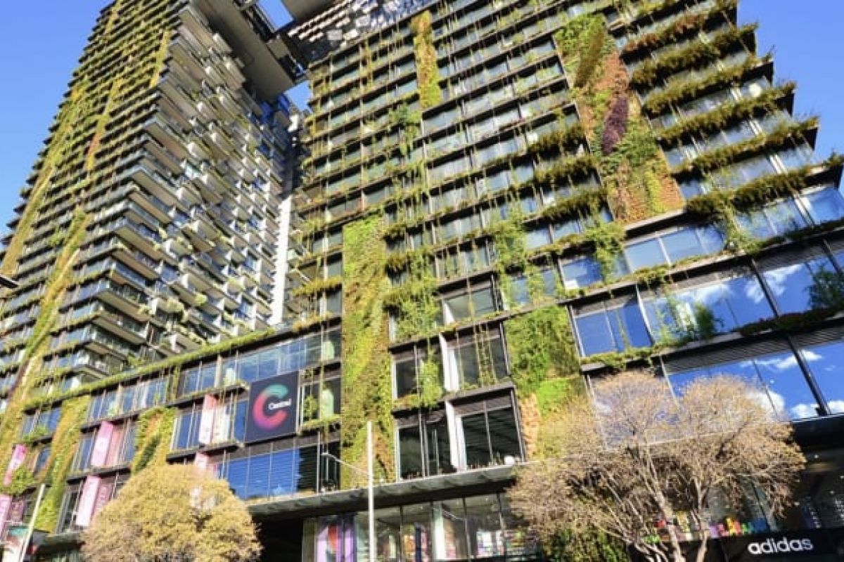 Optima Verdana luxury apartment with Modern building featuring vertical gardens and plants on its facade, showcasing green architecture under a clear blue sky.