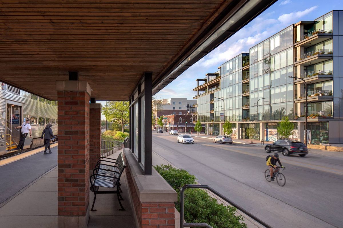 Optima Verdana luxury apartment with A cyclist rides past modern glass buildings as people board a train at a sunny urban station.