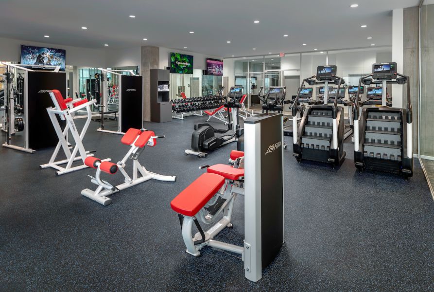 Optima Verdana luxury apartment with Modern gym with red and white exercise machines, treadmills, weights, and TVs on the walls.