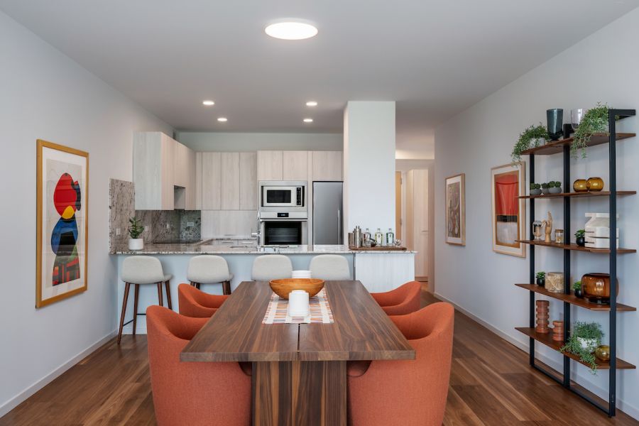 Optima Verdana luxury apartment with Modern dining area with wooden table, orange chairs, open kitchen, and minimalist decor with plants and art.