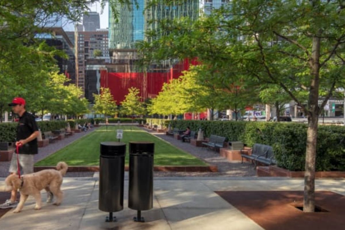 Optima Verdana luxury apartment with A person enjoys a walk with their dog, highlighting pet care in a tree-lined urban park with benches and tall buildings behind.