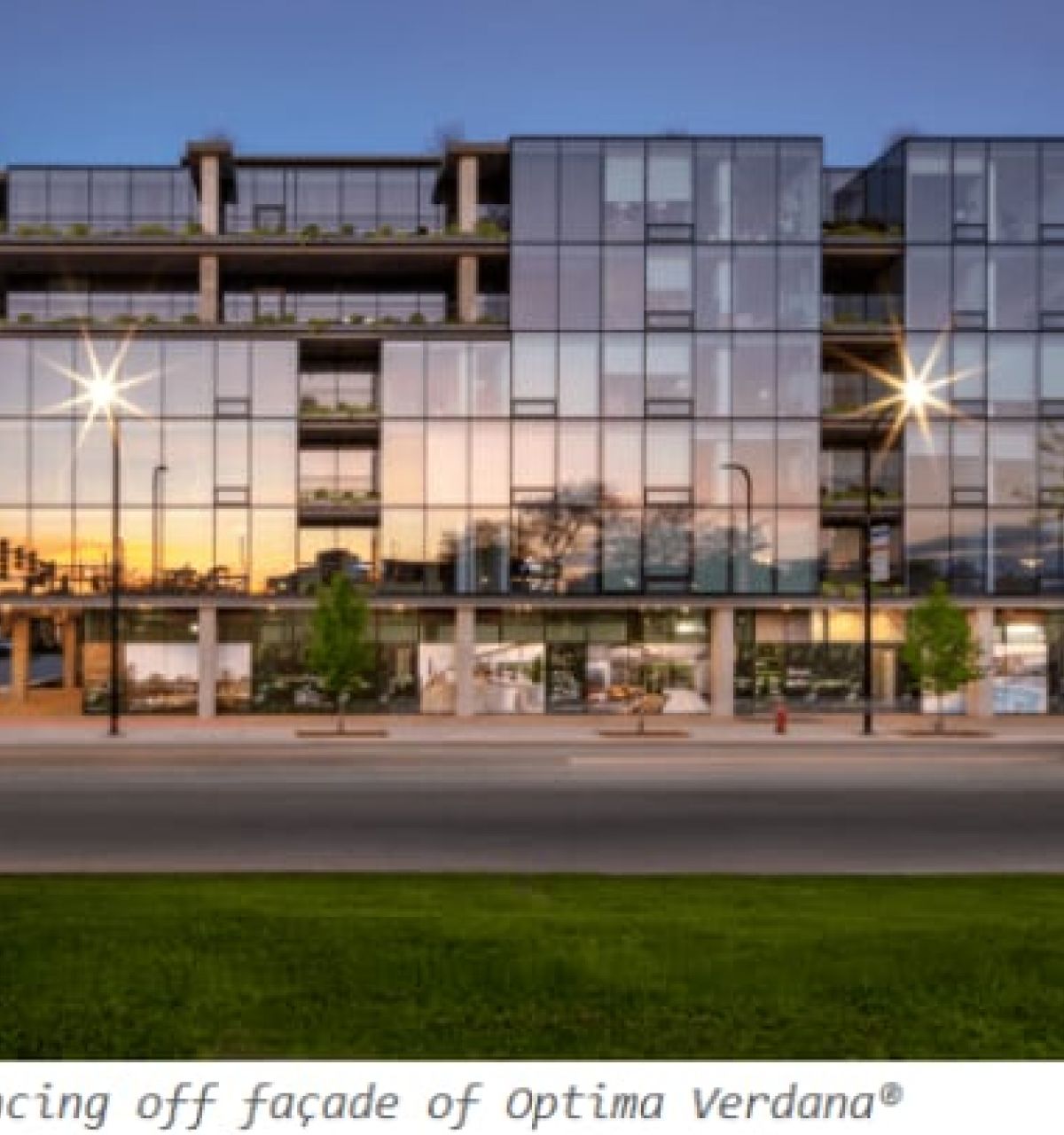 Optima Verdana luxury apartment with A modern glass building reflecting sunrise light, showcasing daylight design and modern architecture, with trees and a quiet street in front.