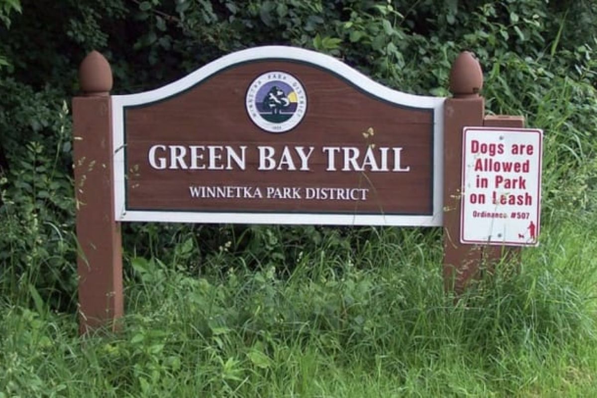 Optima Verdana luxury apartment with Highlights the Green Bay Trail sign, noting leashed dogs are welcome, with Optima Verdana buildings visible amid lush greenery.