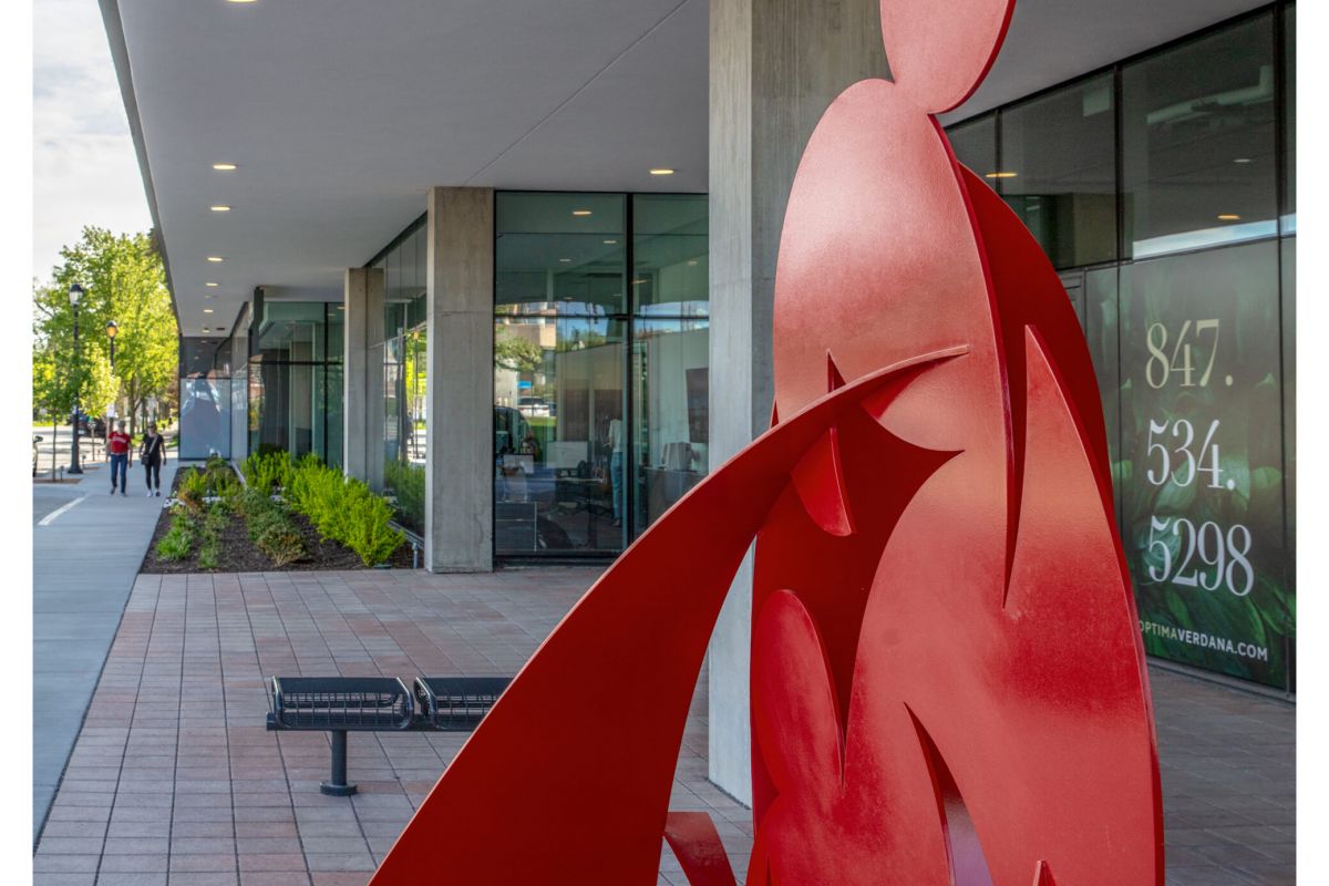 Optima Verdana luxury apartment with Red abstract metal sculpture and modern furniture enhance Optima's Lobbies near a building with large windows and a sidewalk.