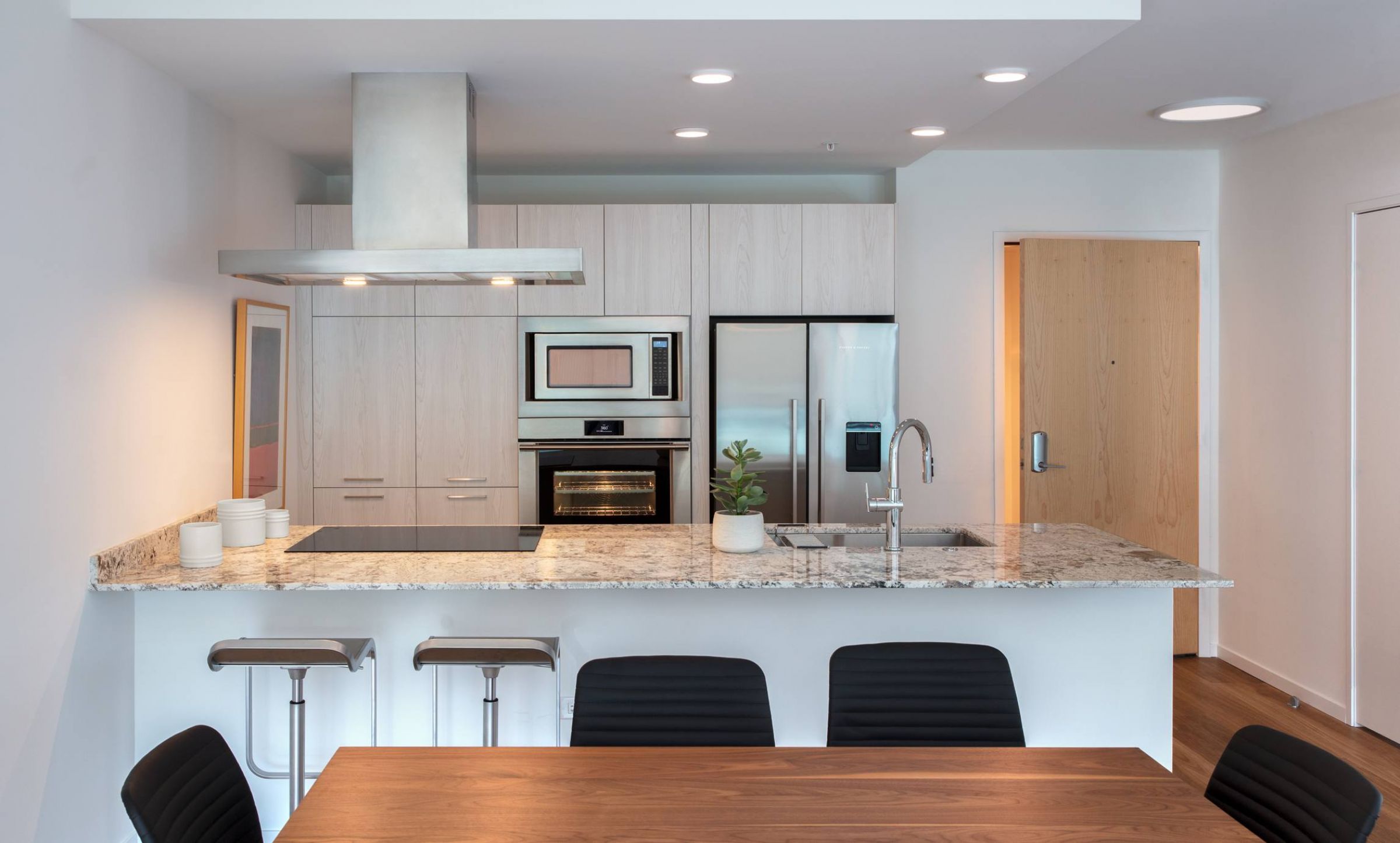 Optima Sonoran Village apartment Modern kitchen with dining table, chairs, barstools, stainless steel appliances, and a plant centerpiece.