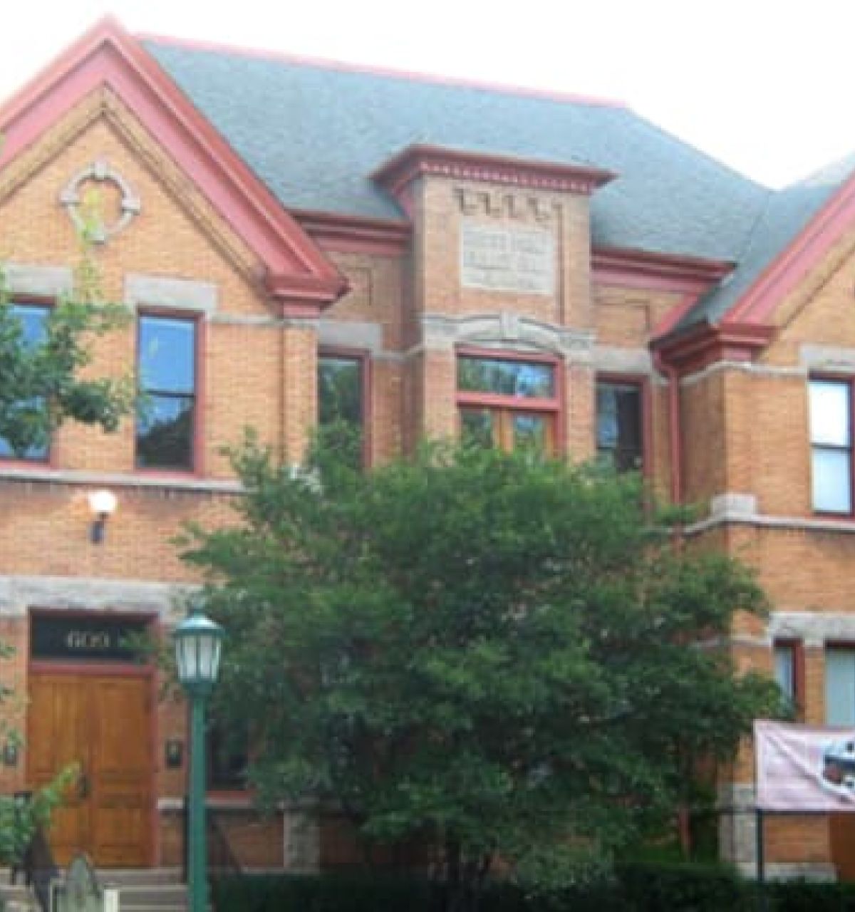 Optima Verdana luxury apartment with A historic two-story brick building in Wilmette with trees in front and a Wilmette Historical Museum banner by the entrance.