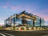 Optima Verdana luxury apartment with Modern glass building at dusk, with people walking on the sidewalk and a clear sky in the background.