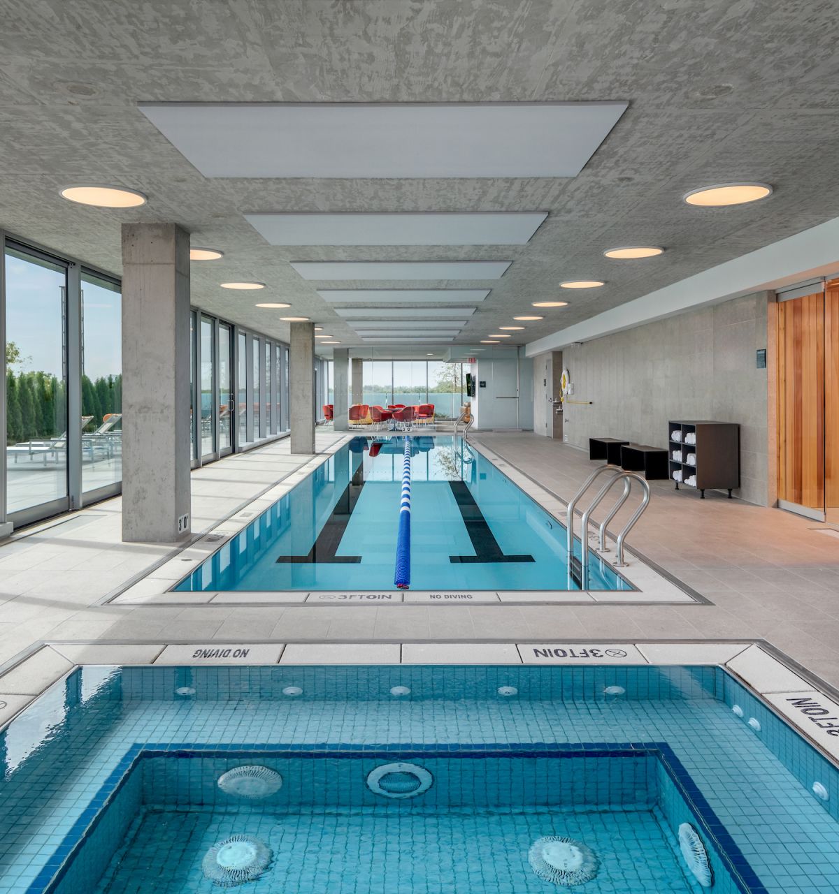 Optima Verdana luxury apartment with Modern indoor pool area with lap pool, hot tub, Recovery Circuit, lounge chairs, large windows, and a sauna room.