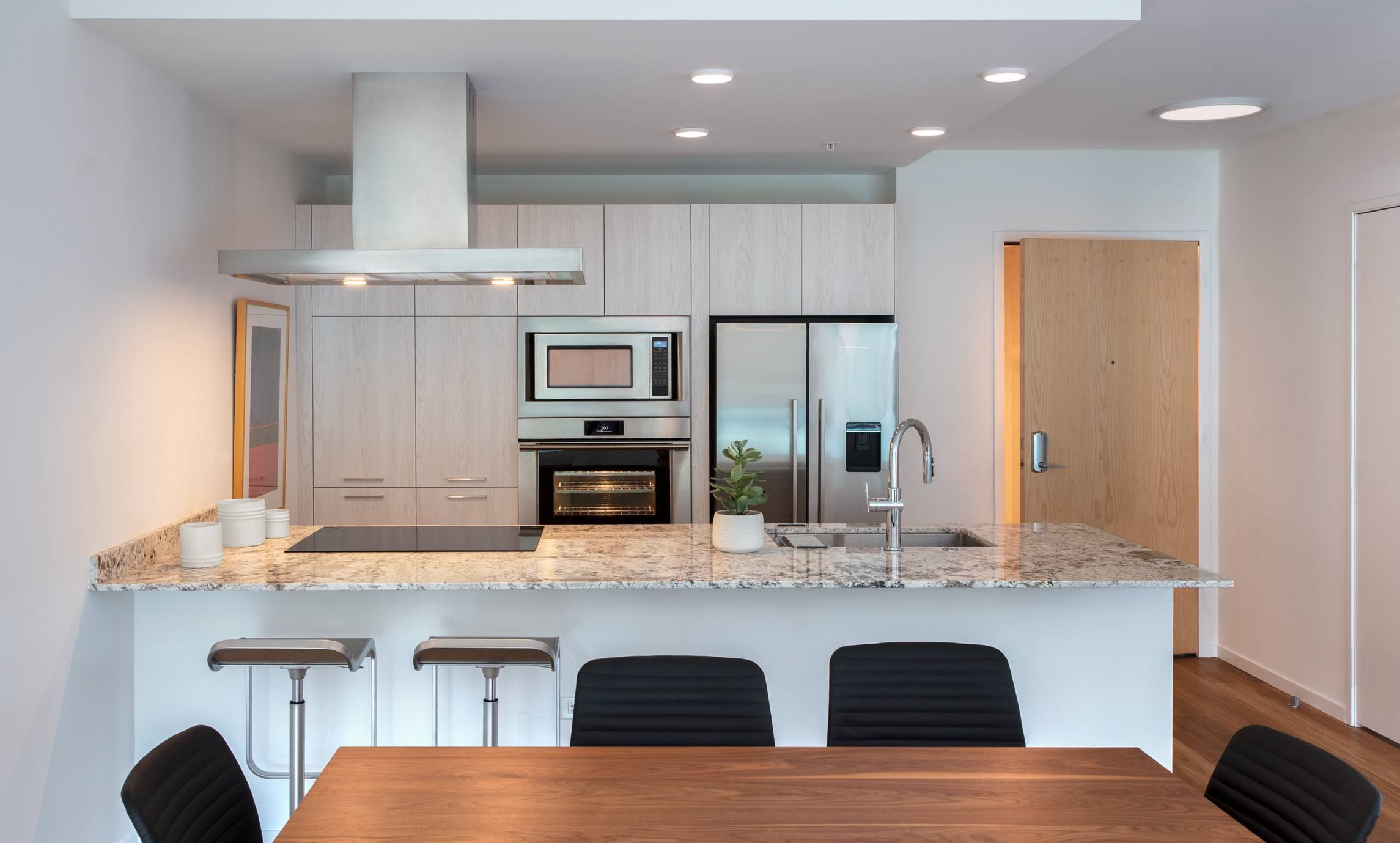 Optima Verdana luxury apartment with Modern kitchen with stainless appliances, marble countertop, bar stools, and a wooden dining table in front.