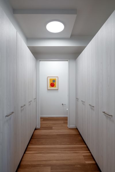 Optima Verdana luxury apartment with A narrow hallway with white cabinets, wooden floor, and a framed abstract artwork at the end.