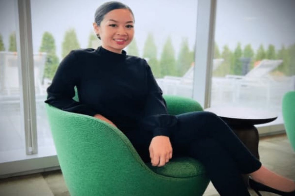 Optima Verdana luxury apartment with Tracy Ratdavong sits smiling on a green chair in a modern, bright indoor space with large Optima Voices windows.