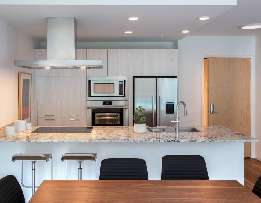 Optima Verdana luxury apartment with Modern kitchen with stainless appliances, marble countertop, bar stools, and a wooden dining table in front.