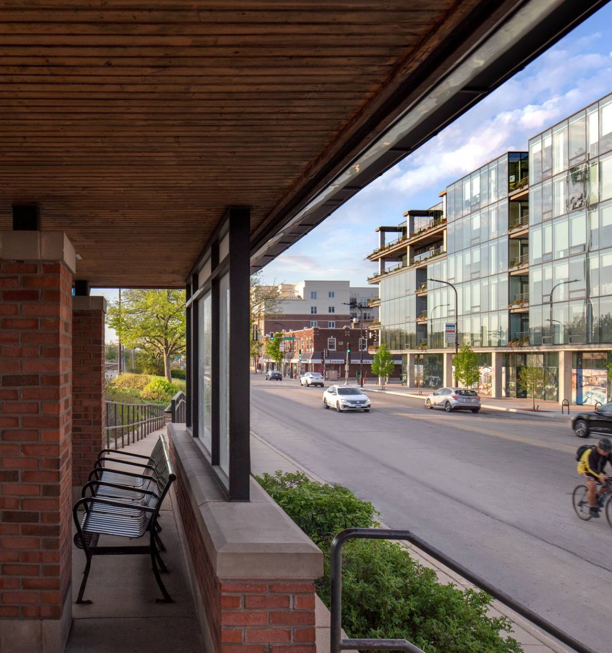 Optima Verdana luxury apartment with A cyclist rides past modern glass buildings as people board a train at a sunny urban station.