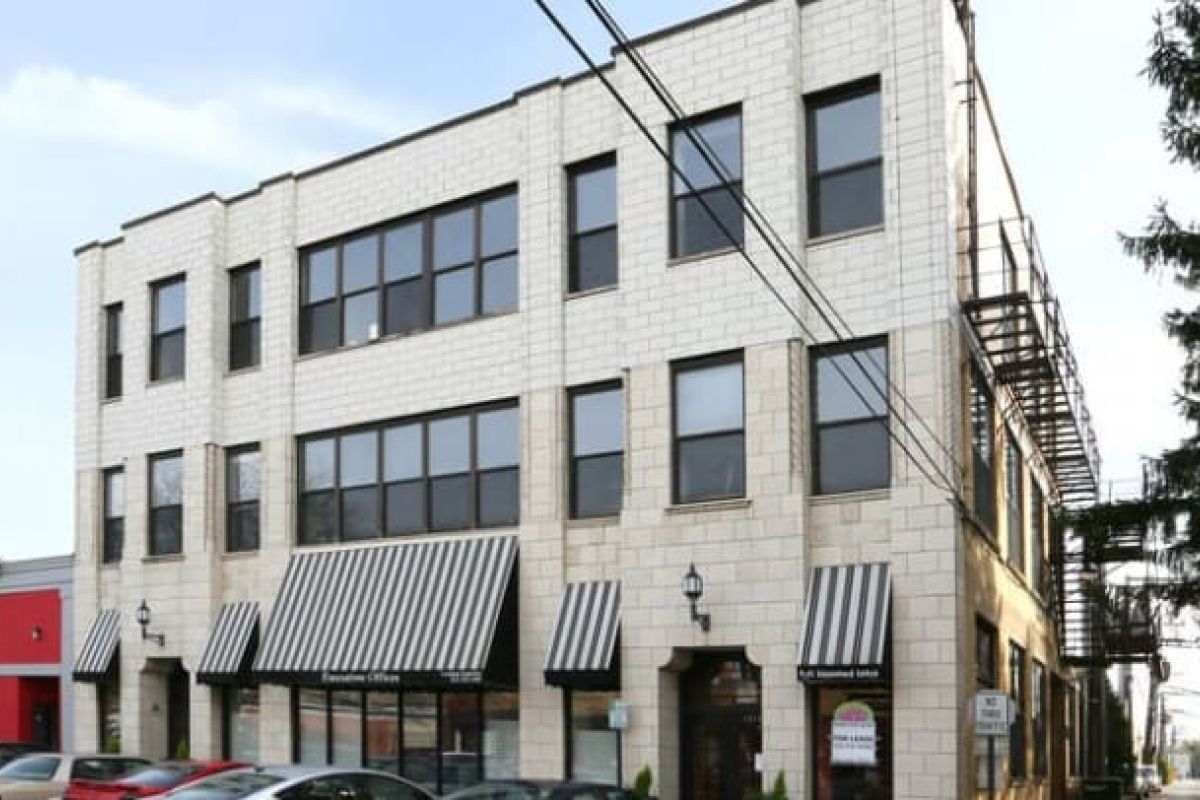 Optima Verdana luxury apartment with Pioneering three-story white brick building with striped awnings in Wilmette, large windows, and cars parked in front.