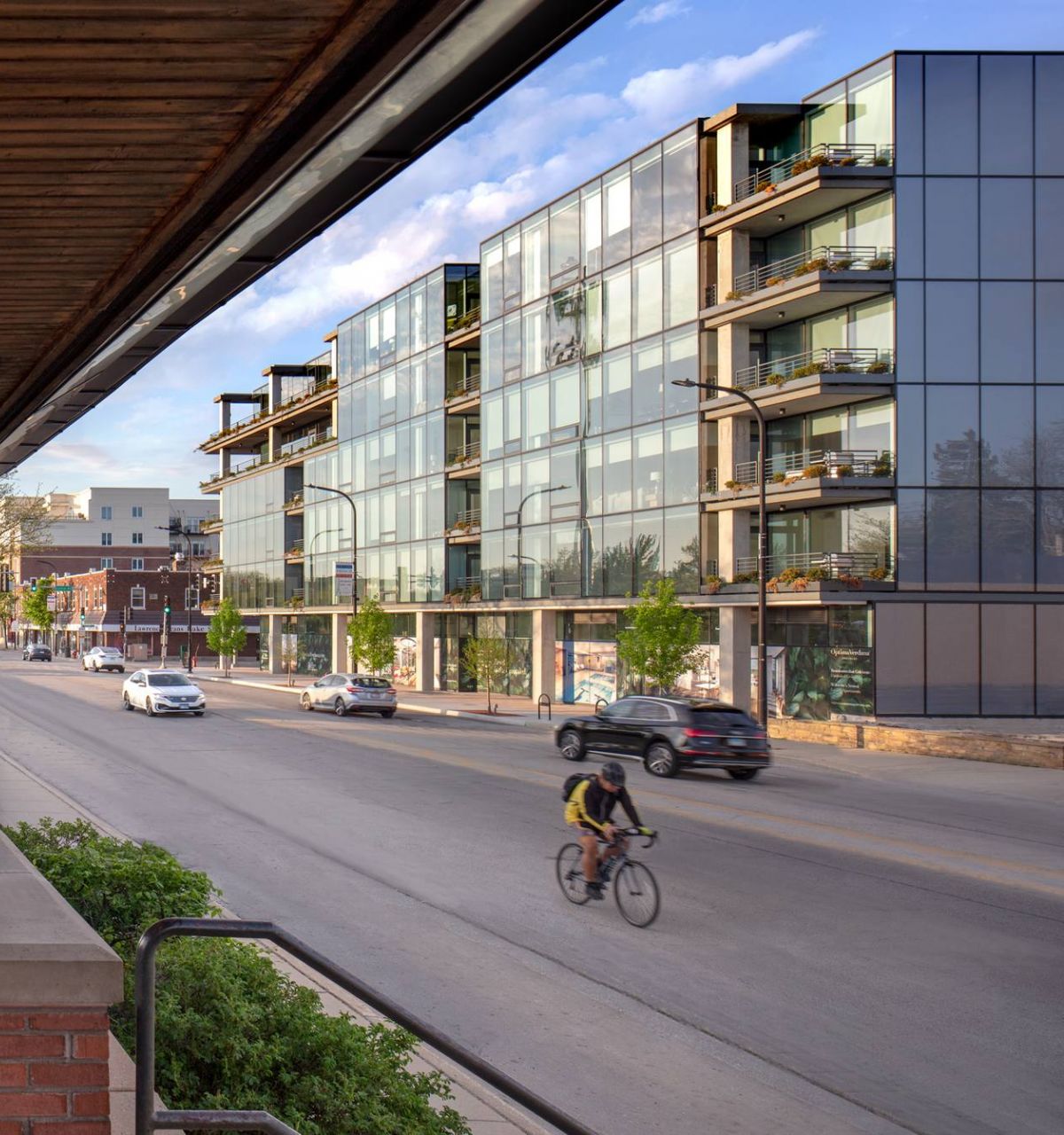 Optima Verdana luxury apartment with A cyclist rides past modern glass apartments and a train station on a sunny city street.