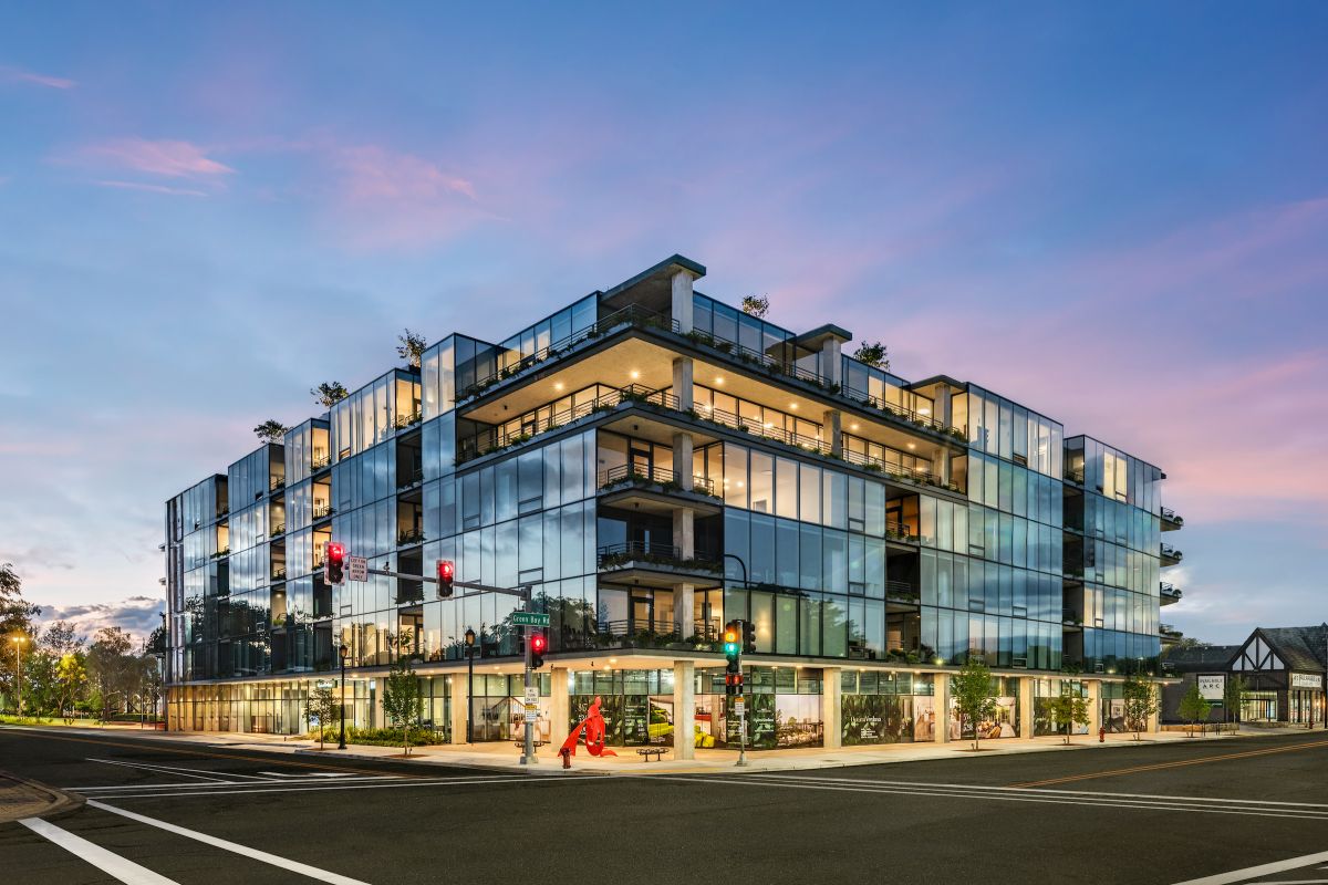 Optima Verdana luxury apartment with Modern glass building at dusk, with people walking on the sidewalk and a clear sky in the background.