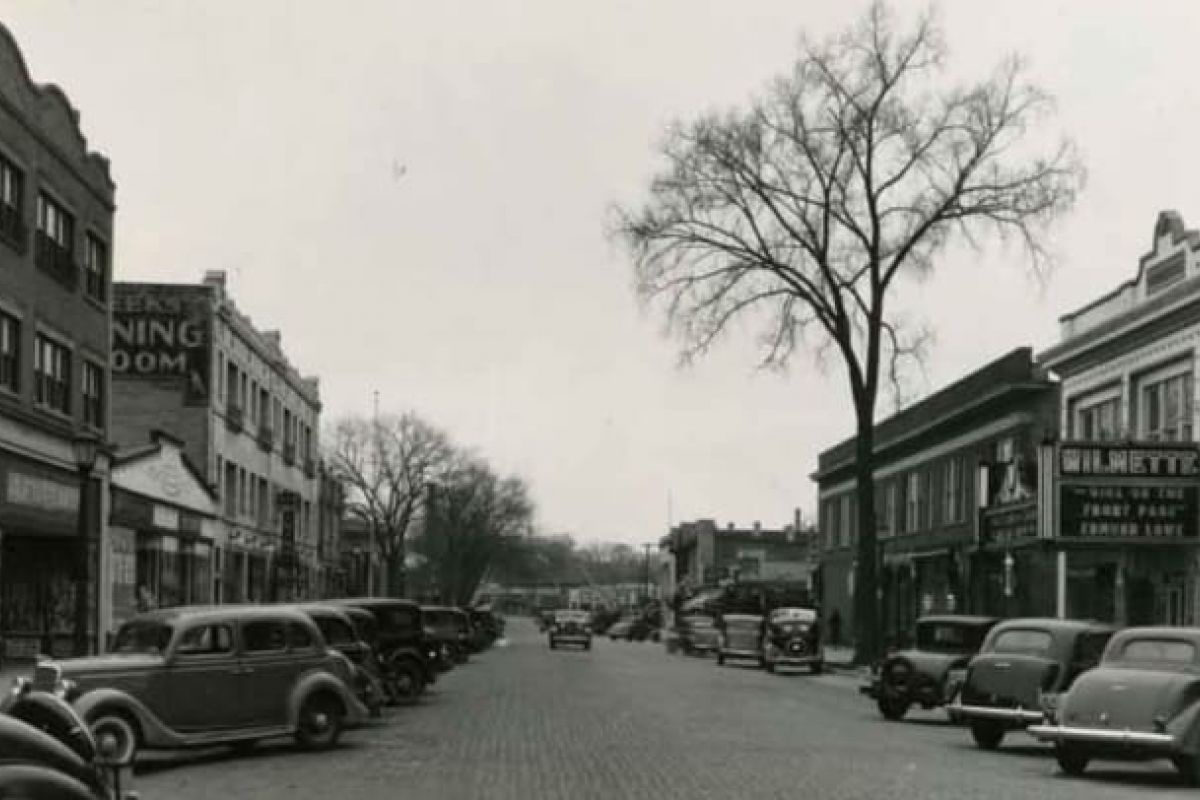 Optima Verdana luxury apartment with Black and white photo of a 1930s Wilmette city street, lined with vintage cars and old storefronts, celebrating its 150th Anniversary.