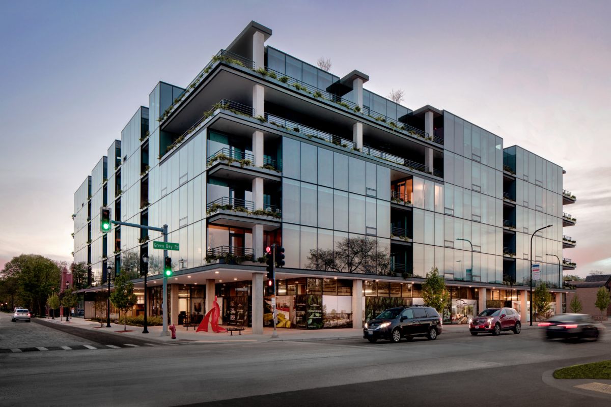 Optima Verdana luxury apartment with Modern glass apartment building with balconies on a city corner at dusk, cars and pedestrians at the intersection.