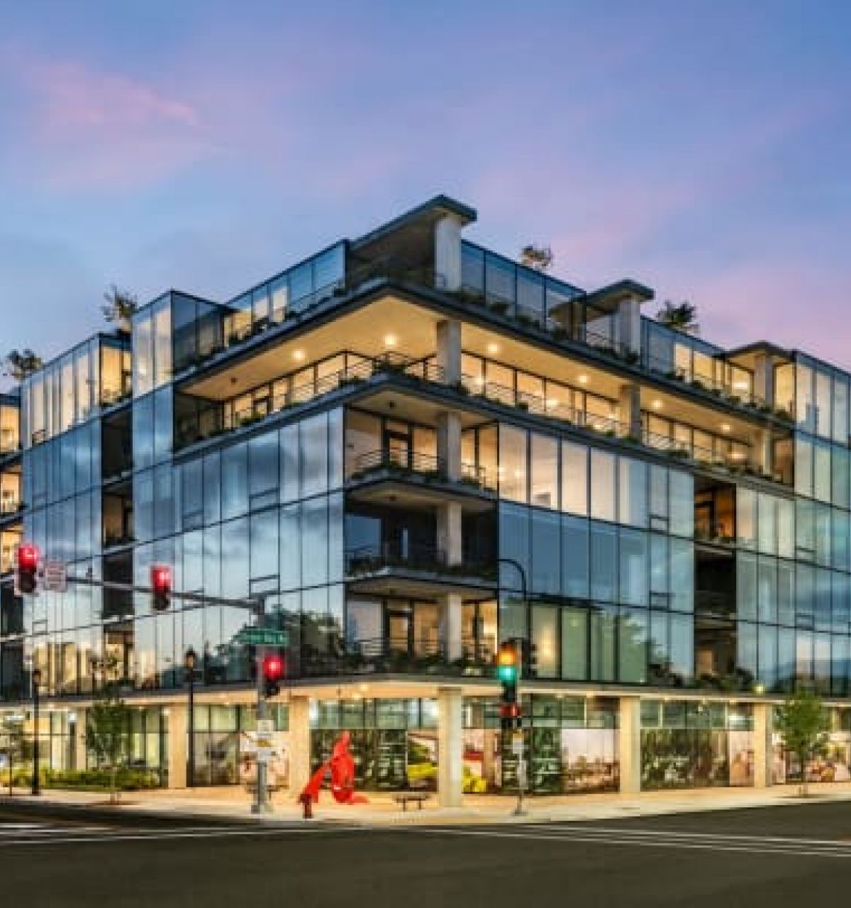 Optima Verdana luxury apartment with Modern glass building at sunset, showcasing Optima Living design as people cross the street at a lively corner intersection.