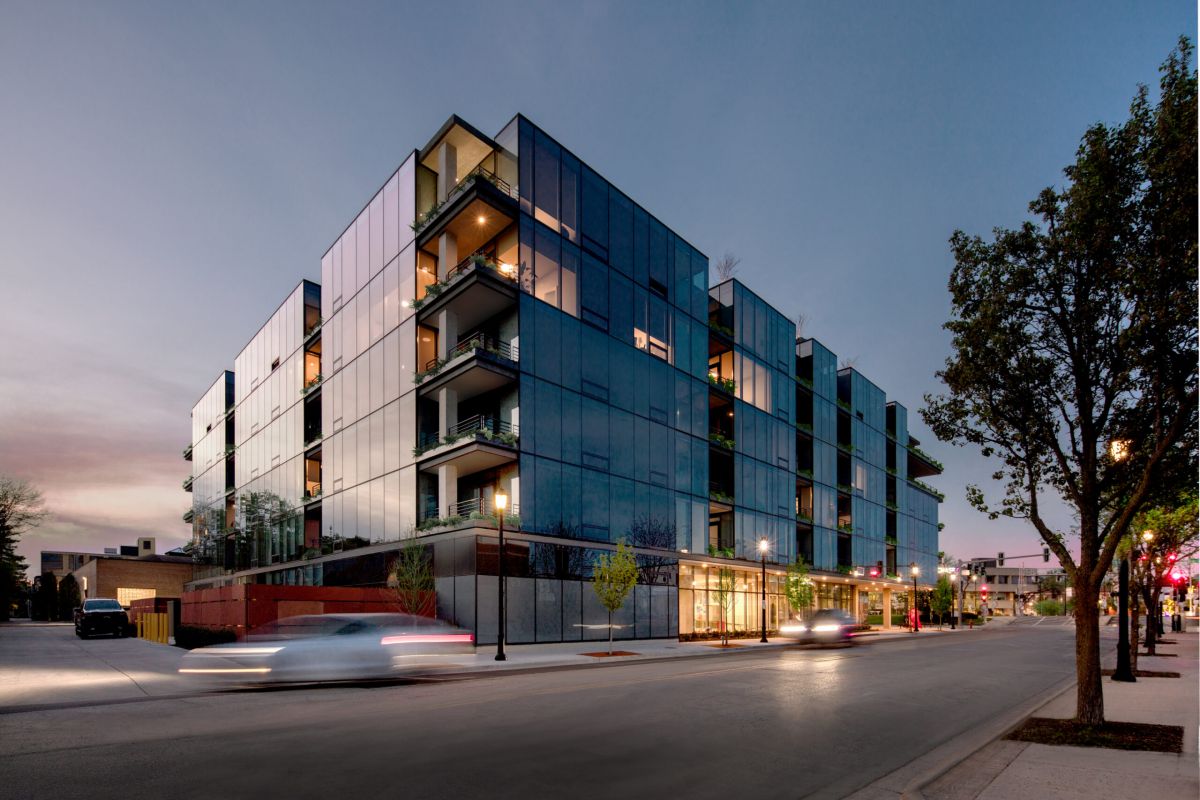 Optima Verdana luxury apartment with Modern glass apartment building at dusk, part of the Optima Community, with cars driving by and tree-lined streets.