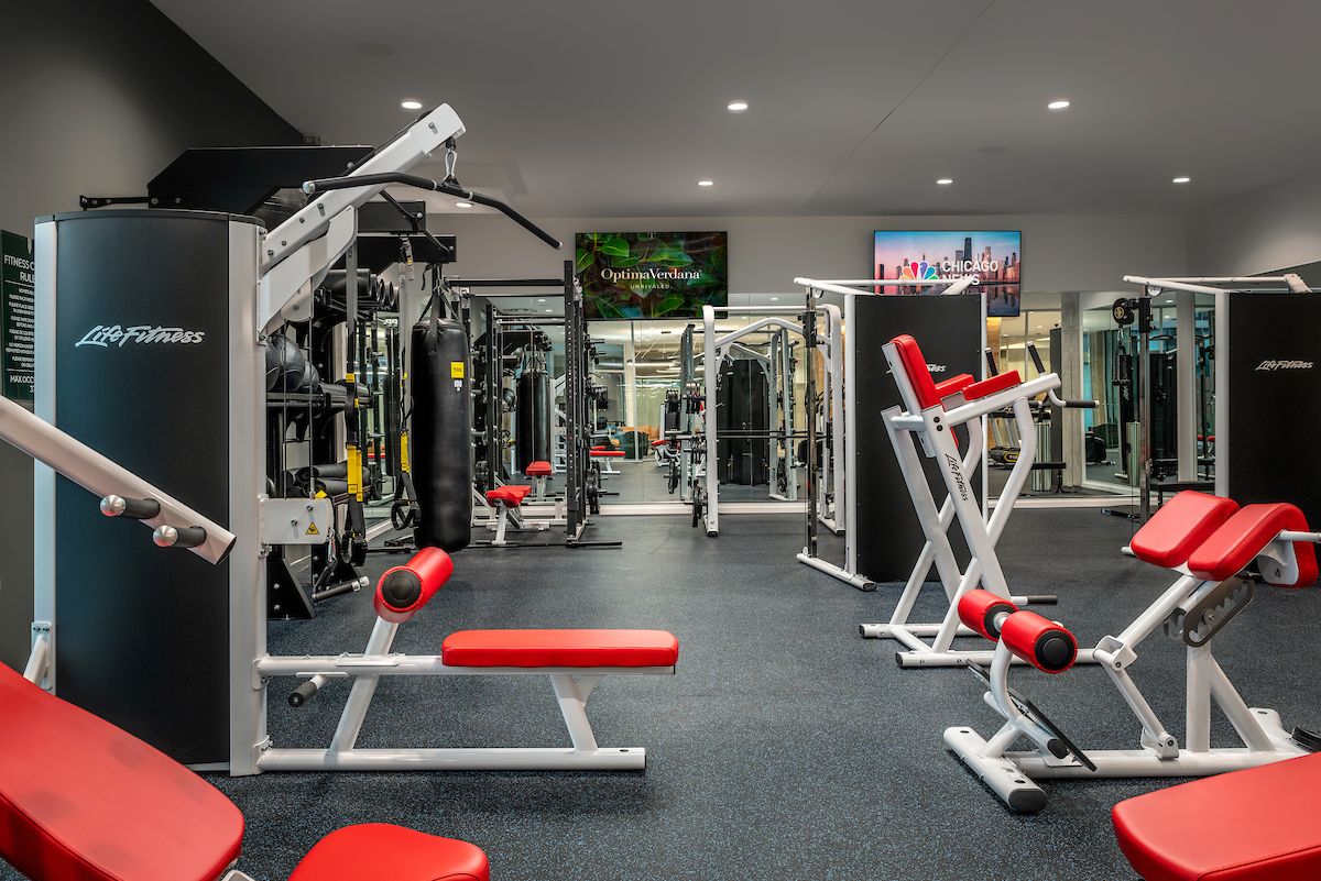 Optima Verdana luxury apartment with Modern gym with red and white exercise machines, weightlifting equipment, and mirrors on the walls.