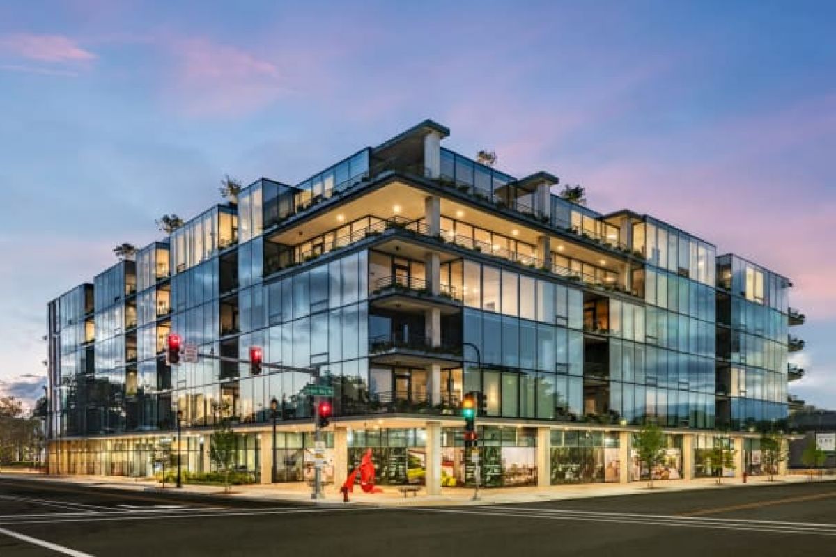 Optima Verdana luxury apartment with Modern glass building at sunset, showcasing Optima Living design as people cross the street at a lively corner intersection.
