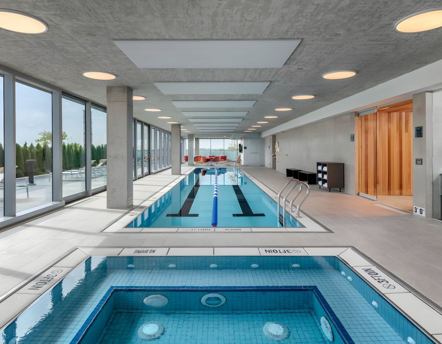 Optima Verdana luxury apartment with Modern indoor pool area with a hot tub in the foreground and large windows along the left side.