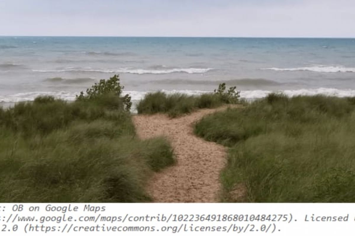 Optima Verdana luxury apartment with A sandy path winds through green dunes at Elmwood Dunes Preserve toward a wavy lake under a cloudy sky.
