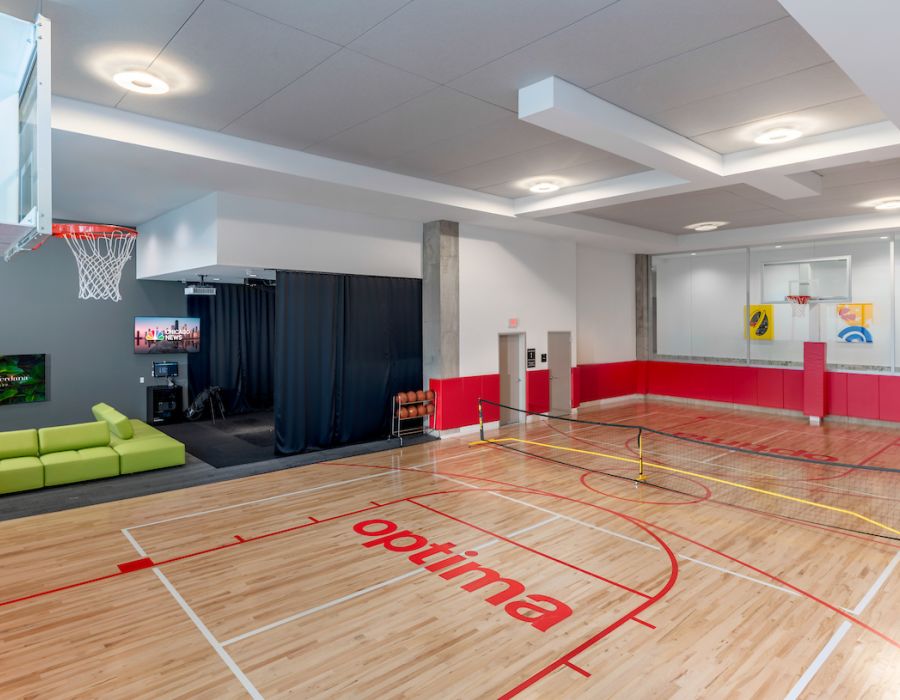Optima Verdana luxury apartment with Indoor gym with a basketball court, net for pickleball, a green couch, and a TV in the corner.