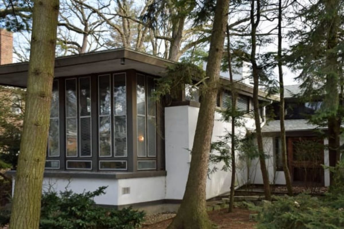 Optima Verdana luxury apartment with A modern house with large vertical windows in Wilmette, inspired by the Frank J. Baker House, surrounded by tall trees and natural landscaping.