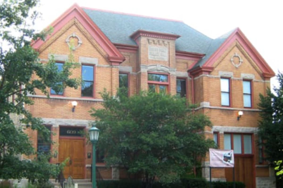 Optima Verdana luxury apartment with A historic two-story brick building in Wilmette with trees in front and a Wilmette Historical Museum banner by the entrance.