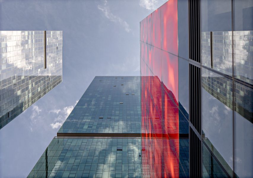 Upward view of modern skyscrapers at Optima Signature apartments with glass reflections, featuring a prominent red facade against a blue sky.
