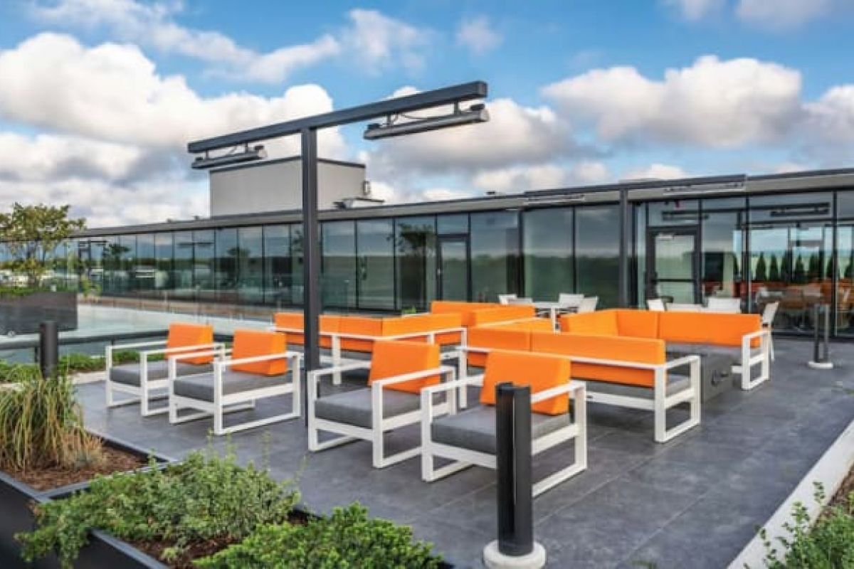 Optima Verdana luxury apartment with Modern rooftop patio with orange and gray seating, glass walls, planters, and the benefits of green roofs under a partly cloudy sky.