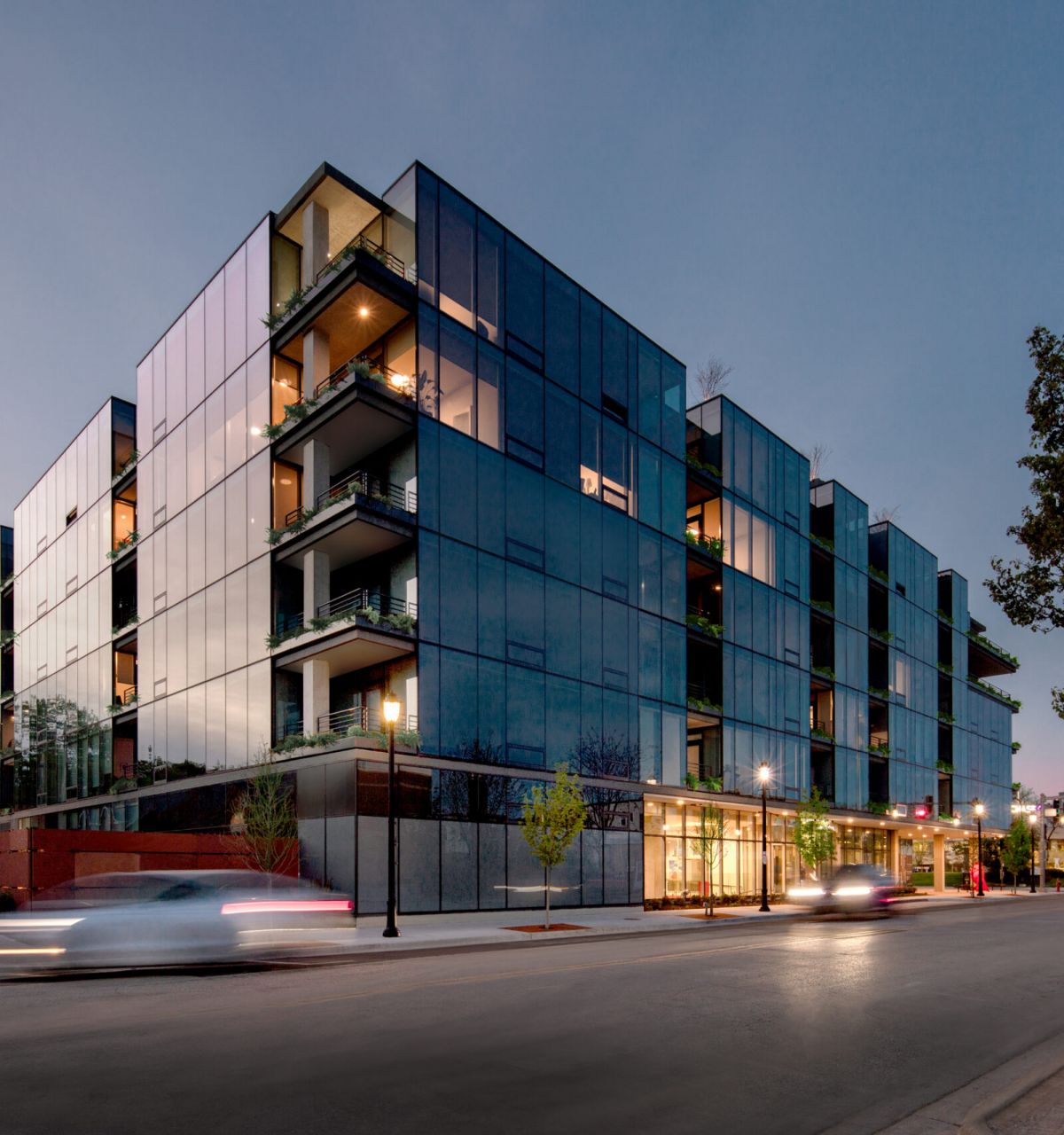 Optima Verdana luxury apartment with Modern glass apartment building at dusk, part of the Optima Community, with cars driving by and tree-lined streets.